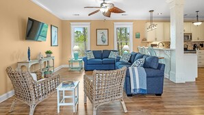 A spacious living room with a large blue sofa, wicker chairs, and a dining area with a table and chairs.