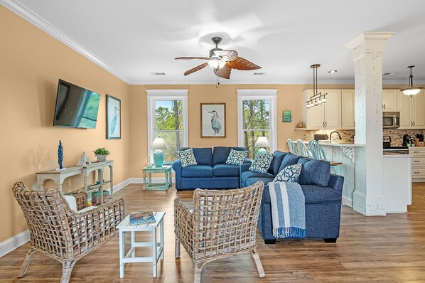 A spacious living room with a large blue sofa, wicker chairs, and a dining area with a table and chairs.