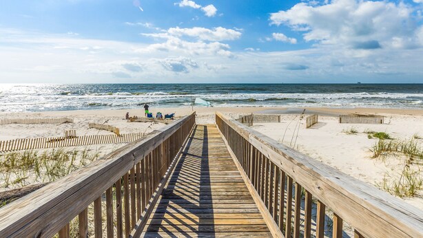 A wooden boardwalk leading to a sandy beach with the ocean in the background.