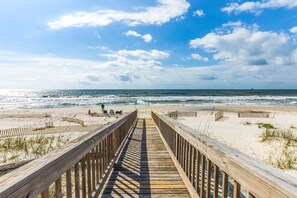 A wooden boardwalk leading to a sandy beach with the ocean in the background.