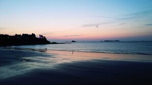 A beach with a calm sea, a distant shoreline with buildings, and a clear sky. - Comfortable apartment 300 m from the beach (Dinard)