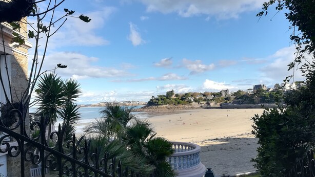 A coastal view with a sandy beach, a decorative fountain, and a stone building in the background. - Comfortable apartment 300 m from the beach (Dinard)