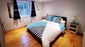 A bedroom with a bed, a window with curtains, a bedside table, and a nightstand. - Comfortable apartment 300 m from the beach (Dinard)
