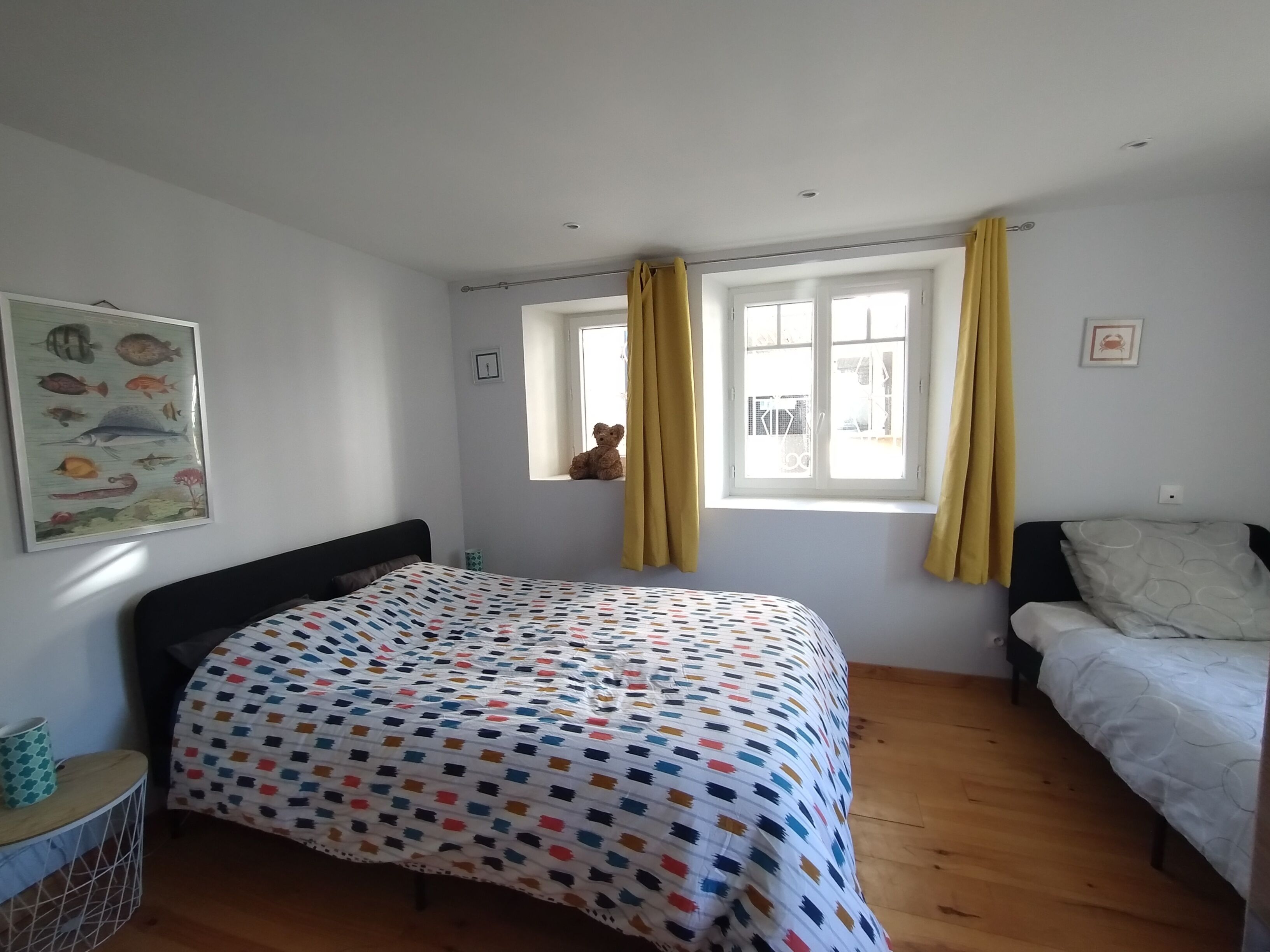 A bedroom with a bed, a window with curtains, a small window with a teddy bear, and a fish poster on the wall.