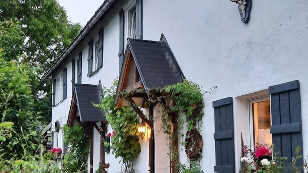 Ein traditionelles Haus mit einem Gartenweg, der zum Eingang führt, ein Hund im Vordergrund und ein Hirschgeweih an der Wand.