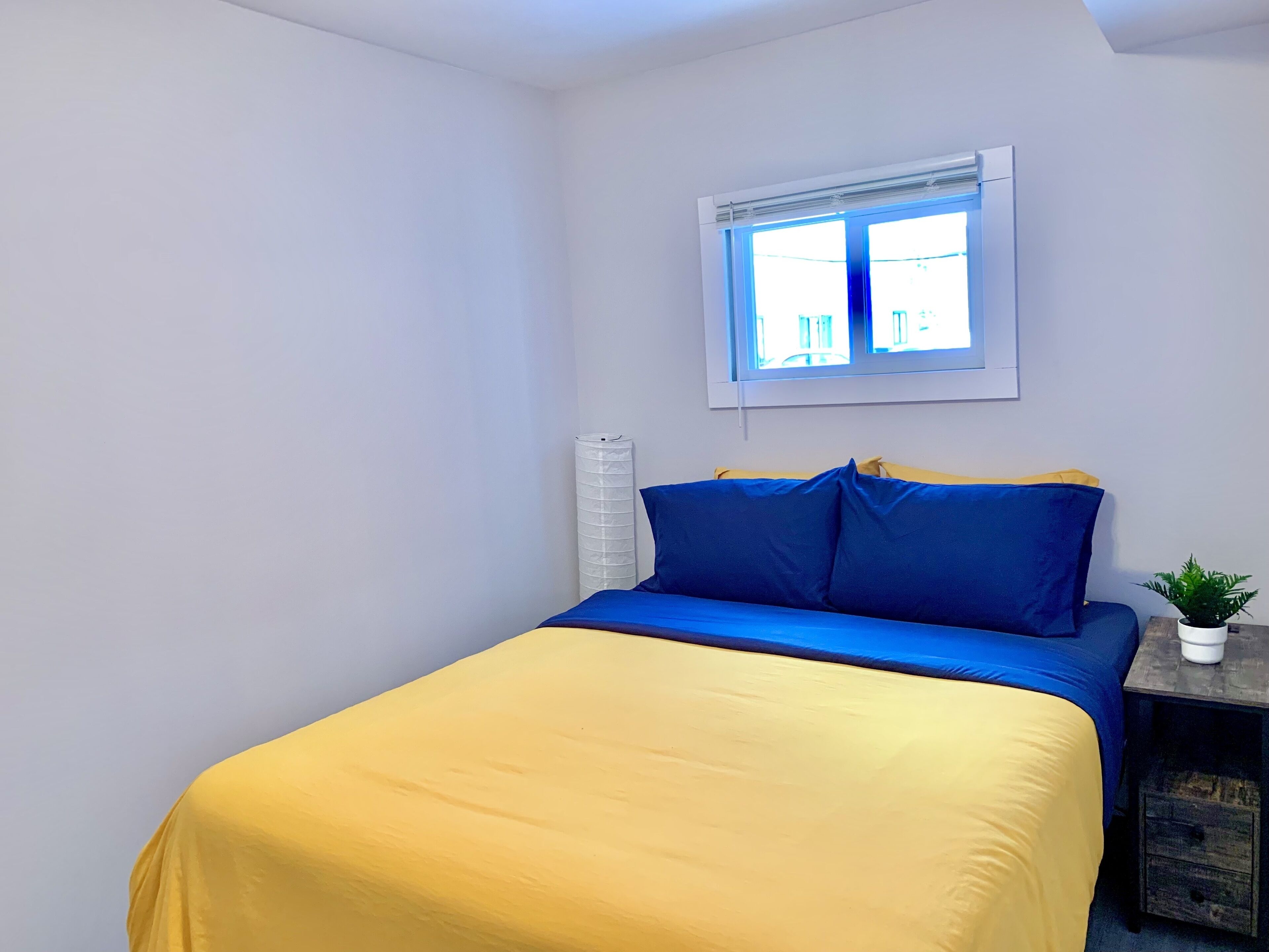 Une chambre à coucher avec un lit, une fenêtre et une petite table sur laquelle est posée une plante.