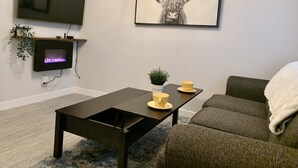 A living room with a flat-screen TV, a fireplace, a coffee table, a sofa, and a framed artwork of a bull. - Cozy Downtown Suite - Walking Distance to Restaurants & shops - Quiet Area (Golden)