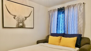 A bedroom with a bed, a headboard, a pillow, a blanket, a wall-mounted picture, and a window with curtains. - Cozy Downtown Suite - Walking Distance to Restaurants & shops - Quiet Area (Golden)