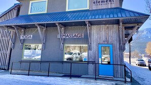 A building with signs for 'Yoga' and 'Massage' services, a wooden facade, and a blue door. - Cozy Downtown Suite - Walking Distance to Restaurants & shops - Quiet Area (Golden)