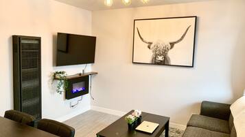A modern living room with a flat-screen TV, a fireplace, a sofa, a coffee table, and a framed artwork of a bull's head.