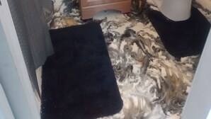 Ein Badezimmer mit einer Wand im Marmor-Muster, einem Holzschrank, einer Toilette und einem schwarzen Teppich.