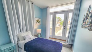 A bedroom with a bed, a nightstand, a lamp, a window with curtains, and a view of the outside. - Beach, beach, in historic Cape Charles. Lovely 2BR Apt. 1 Block from beach (Cape Charles)