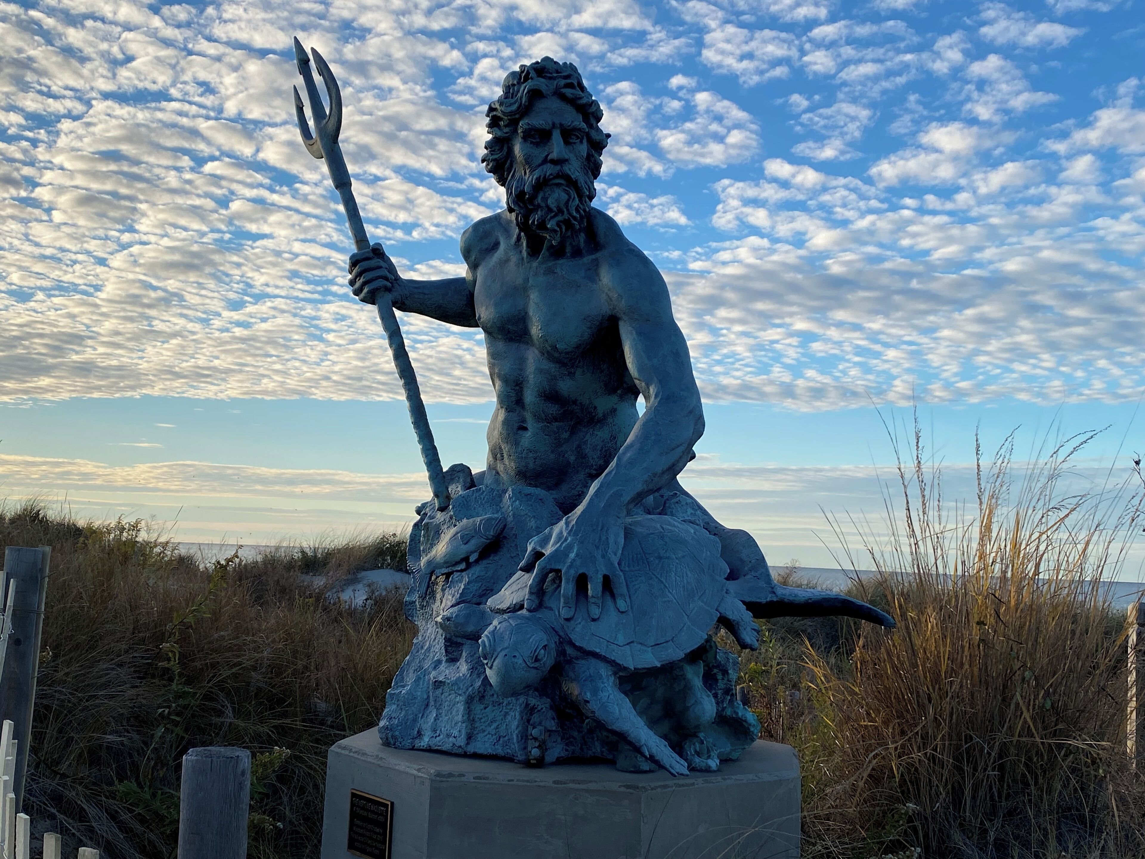 Una estatua de un hombre barbudo sosteniendo un tridente, sentado sobre una roca con un pez.