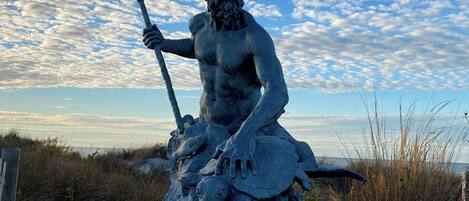 Una estatua de un hombre barbudo sosteniendo un tridente, sentado sobre una roca con un pez.