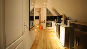 A modern kitchen with wooden flooring, stainless steel appliances, and a white refrigerator. - Vacation apartment in a half-timbered house (Jonsdorf)