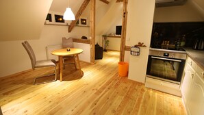 A cozy kitchen with wooden floors, a dining area with a table and chairs, and a modern oven. - Vacation apartment in a half-timbered house (Jonsdorf)