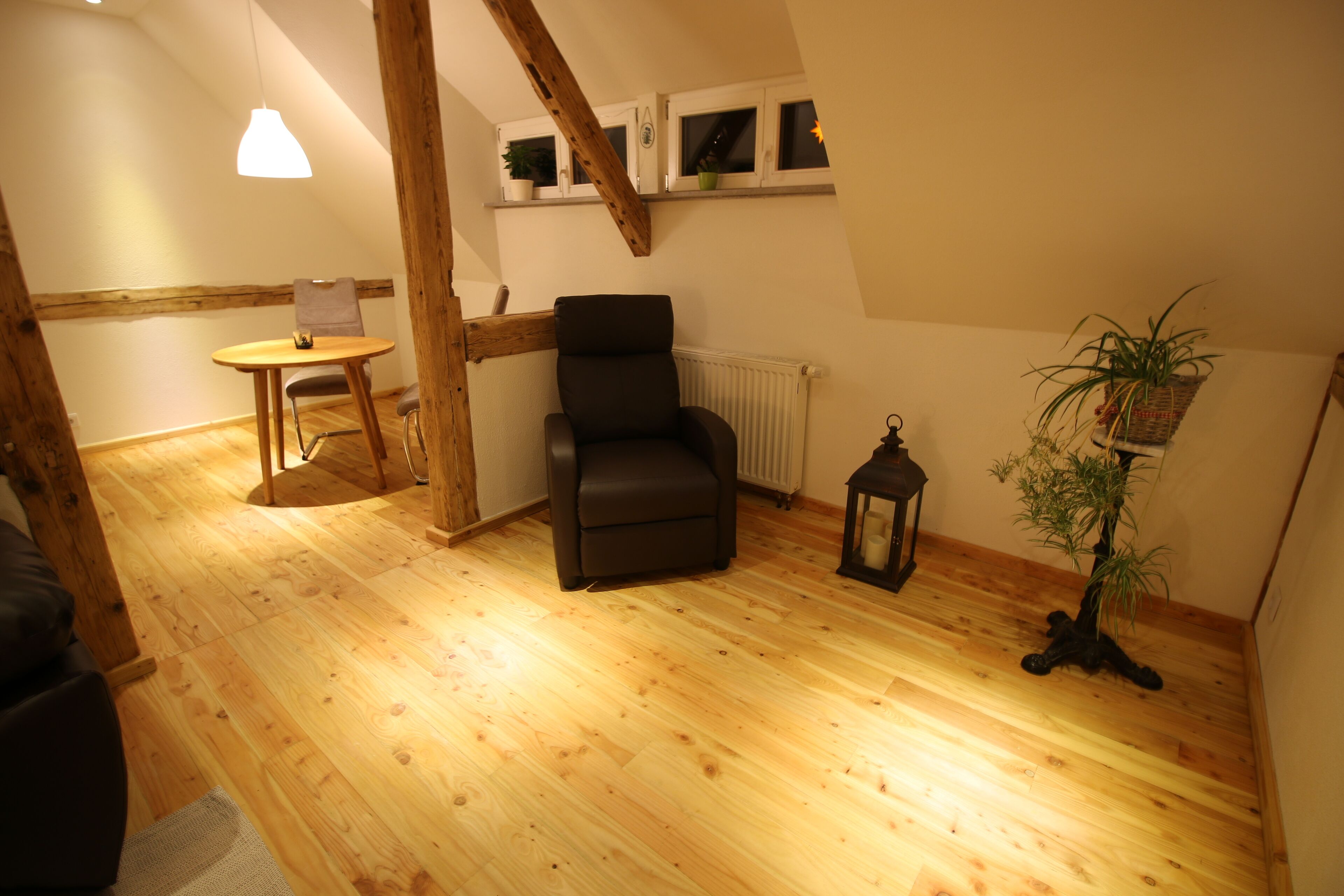 A cozy room with wooden flooring, a black chair, a small table, and a potted plant.