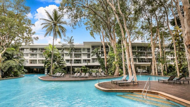 A pool area with lounge chairs and a building with multiple balconies in the background.