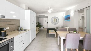 A modern kitchen with white cabinets, a built-in stove, and a sink. There is a dining area with a table and chairs, and a living space with a sofa and a coffee table.
