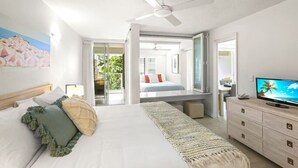 A bedroom with a bed, a TV, a ceiling fan, and a view of the outdoors.