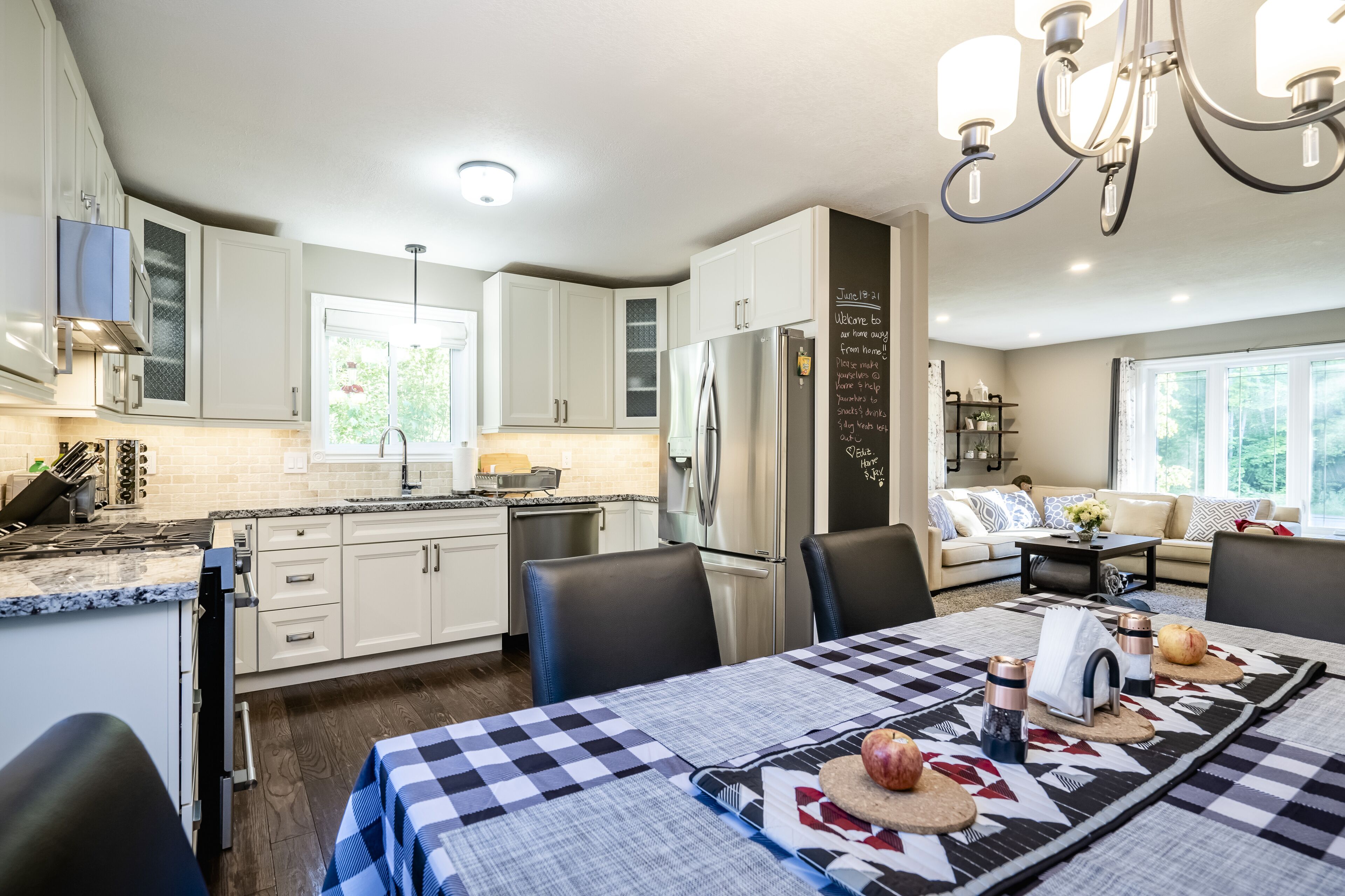 A modern kitchen with white cabinets, a stainless steel refrigerator, and a dining area with a checkered tablecloth.