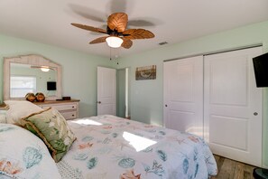 A bedroom with a bed, a ceiling fan, a dresser, a mirror, and a closet.