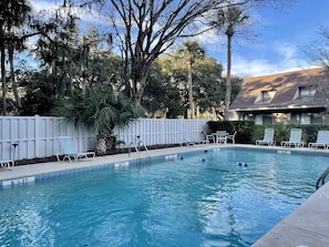 Relax by the serene pool surrounded by lush greenery and a white picket fence.