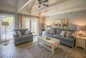 Relax in this spacious living room with a high ceiling and exposed beams, featuring a cozy seating area and adjustable lighting options.