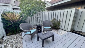 Eine Terrasse mit zwei Korbstühlen und einem kleinen Tisch, umgeben von einem Holzzaun und einer großen Pflanze.