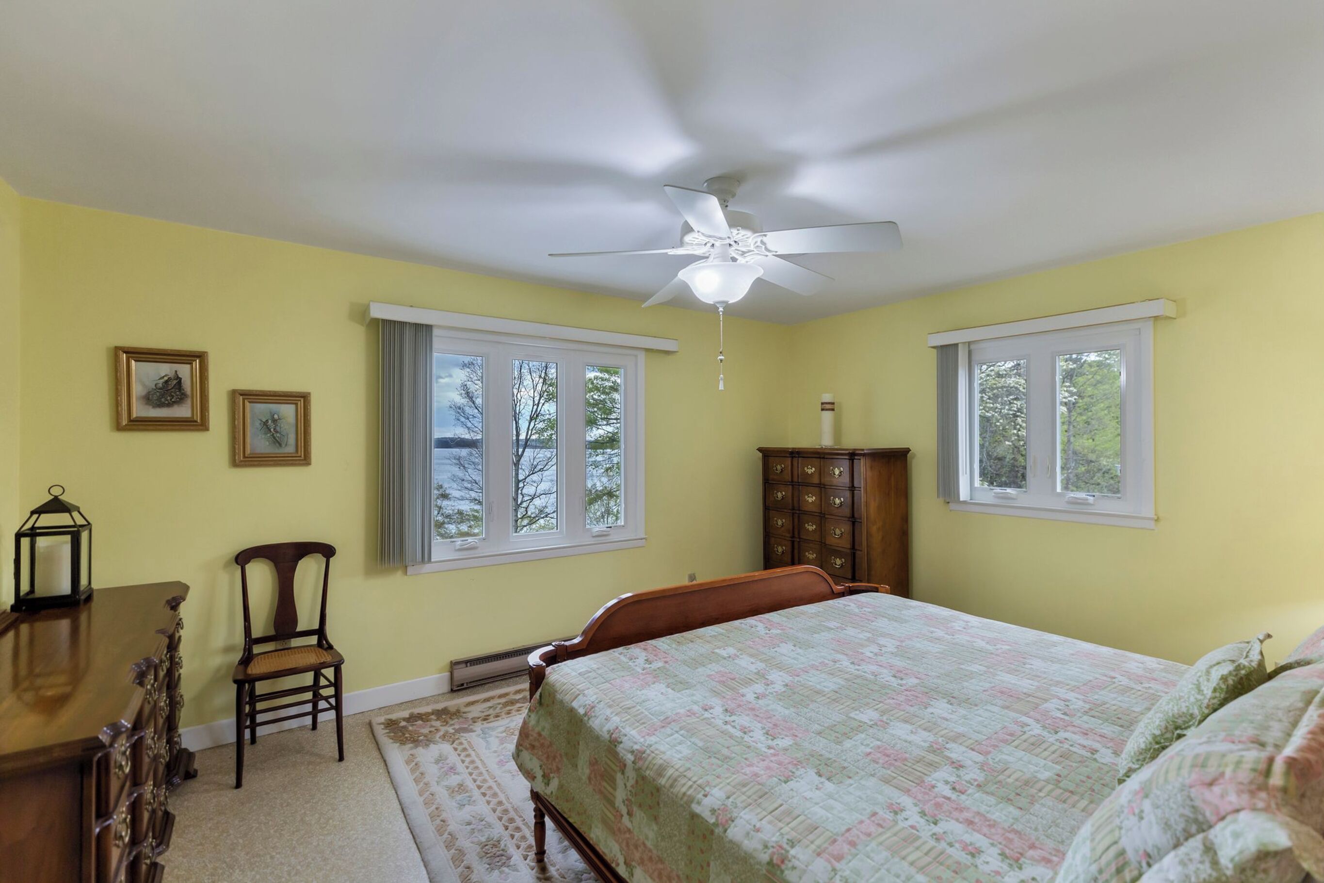 A bedroom with a bed, a ceiling fan, two windows, a dresser, and a chair.