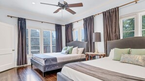 Ein Schlafzimmer mit zwei Betten, einem Deckenventilator, großen Fenstern und Blick ins Freie.