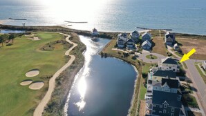 An aerial view of a coastal residential area with a golf course, a body of water, and houses with a large arrow pointing to one house. - Gorgeous 4BR Home With Panoramic Sunsets & Walking Distance to Private Beach! (Cape Charles)