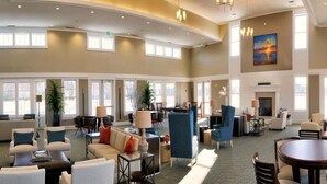 A spacious lobby with multiple seating areas, a fireplace, and large windows allowing natural light. - Gorgeous 4BR Home With Panoramic Sunsets & Walking Distance to Private Beach! (Cape Charles)