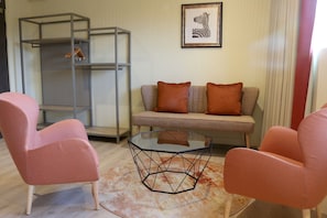 Un salon comprenant un canapé, deux fauteuils, une table basse en verre et une étagère en métal.