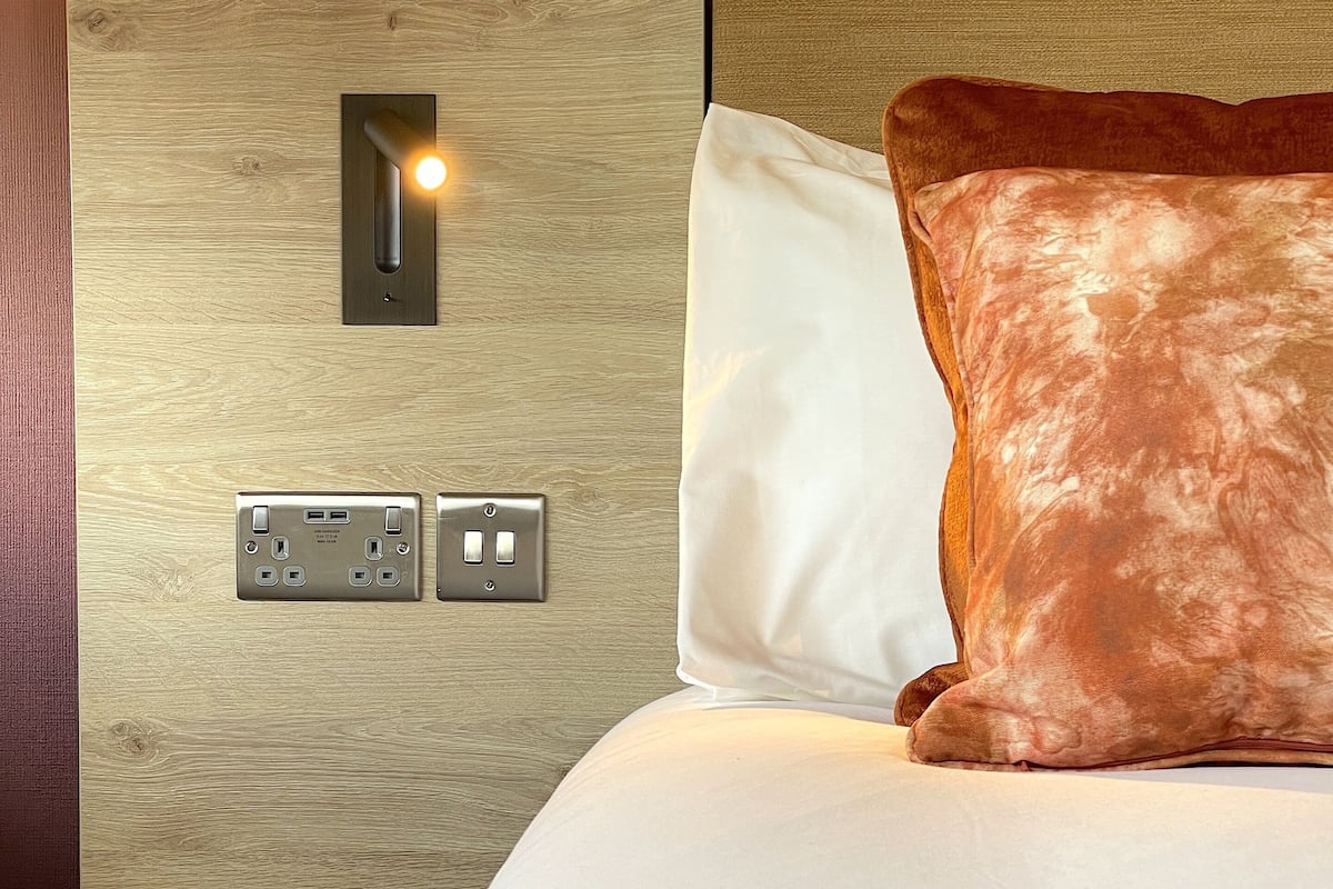A bed with a wooden headboard, a power outlet, and a light switch.
