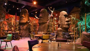 A restaurant with round tables, chairs, and a tropical theme with large rock sculptures and plants. - Hex Wildlife Hotel (Doncaster)