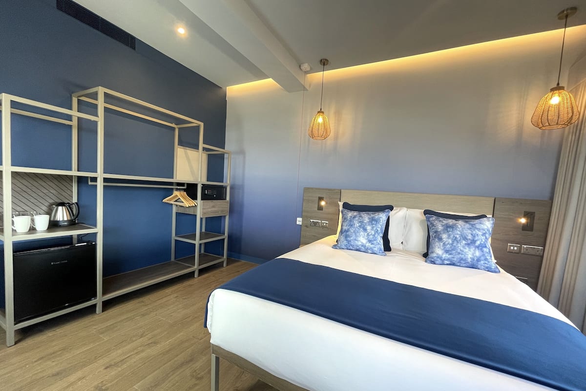A modern hotel room with a bed, a built-in wardrobe, and a small kitchenette.