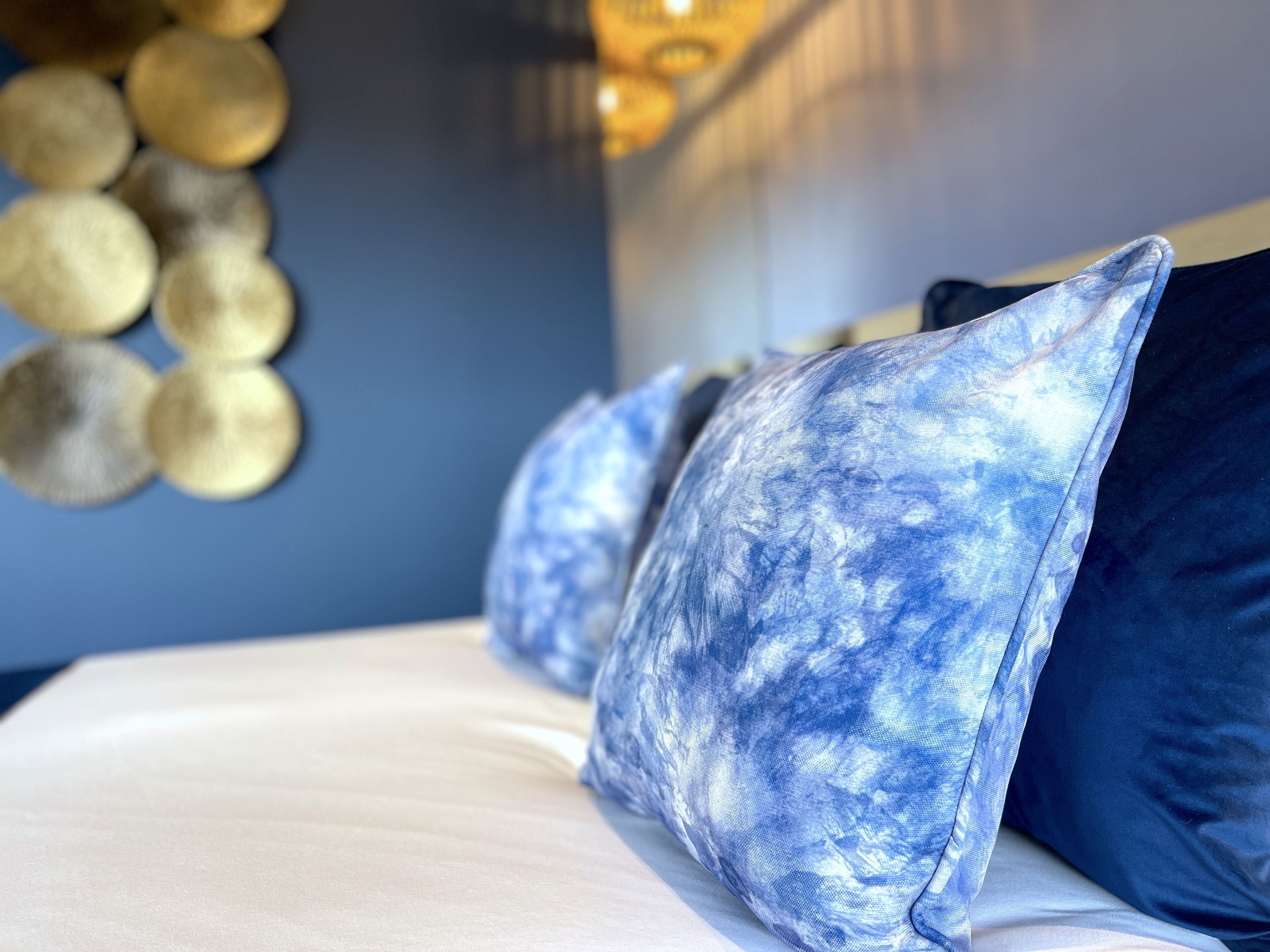 Una cama con sábana blanca y almohadas estampadas en azul.