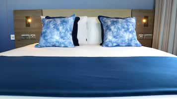 Una cama con colcha azul y dos almohadas a juego, cabecera de madera y luces de lectura fijadas a la pared.