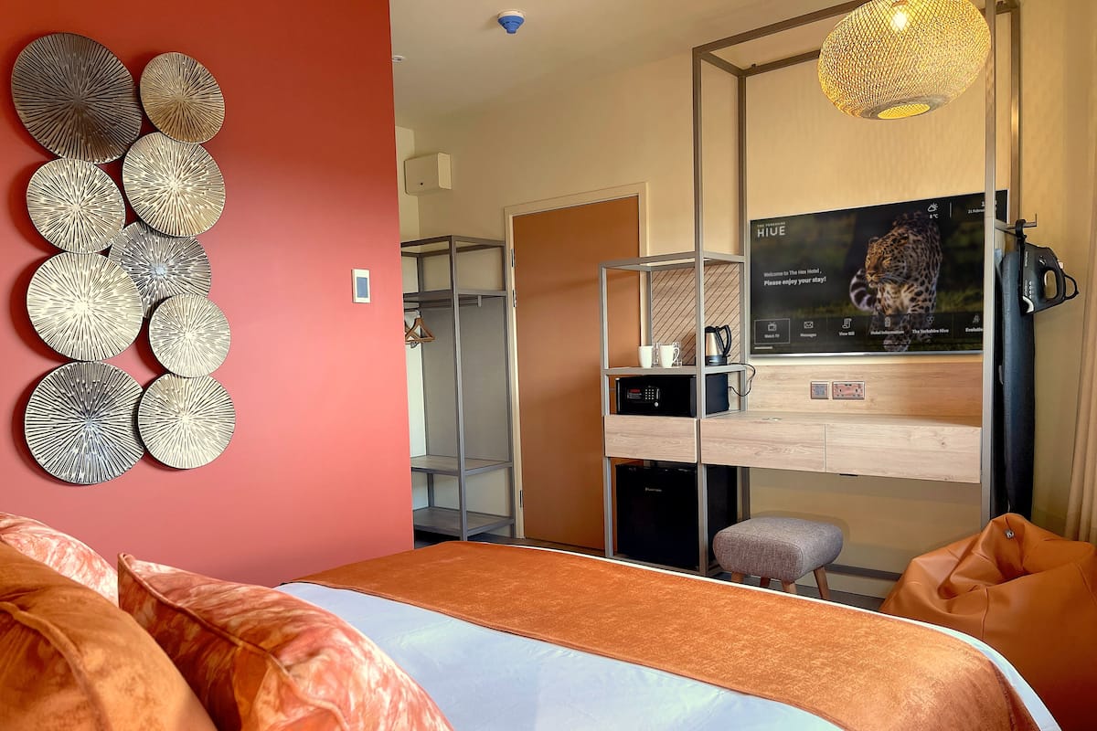 A modern hotel room with a bed, a wardrobe, a TV, and a decorative wall piece.