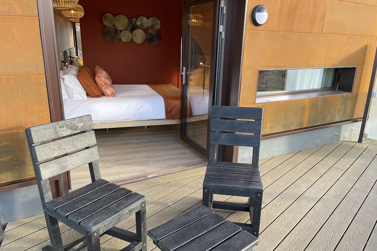 A cozy bedroom with a bed, a wooden bench, and a chair on a wooden deck.
