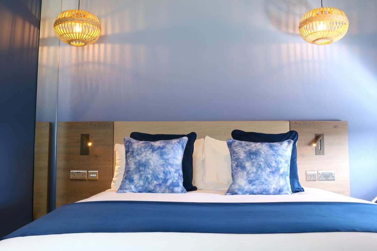 A hotel room with a large bed, two wall-mounted light fixtures, and a wooden headboard.