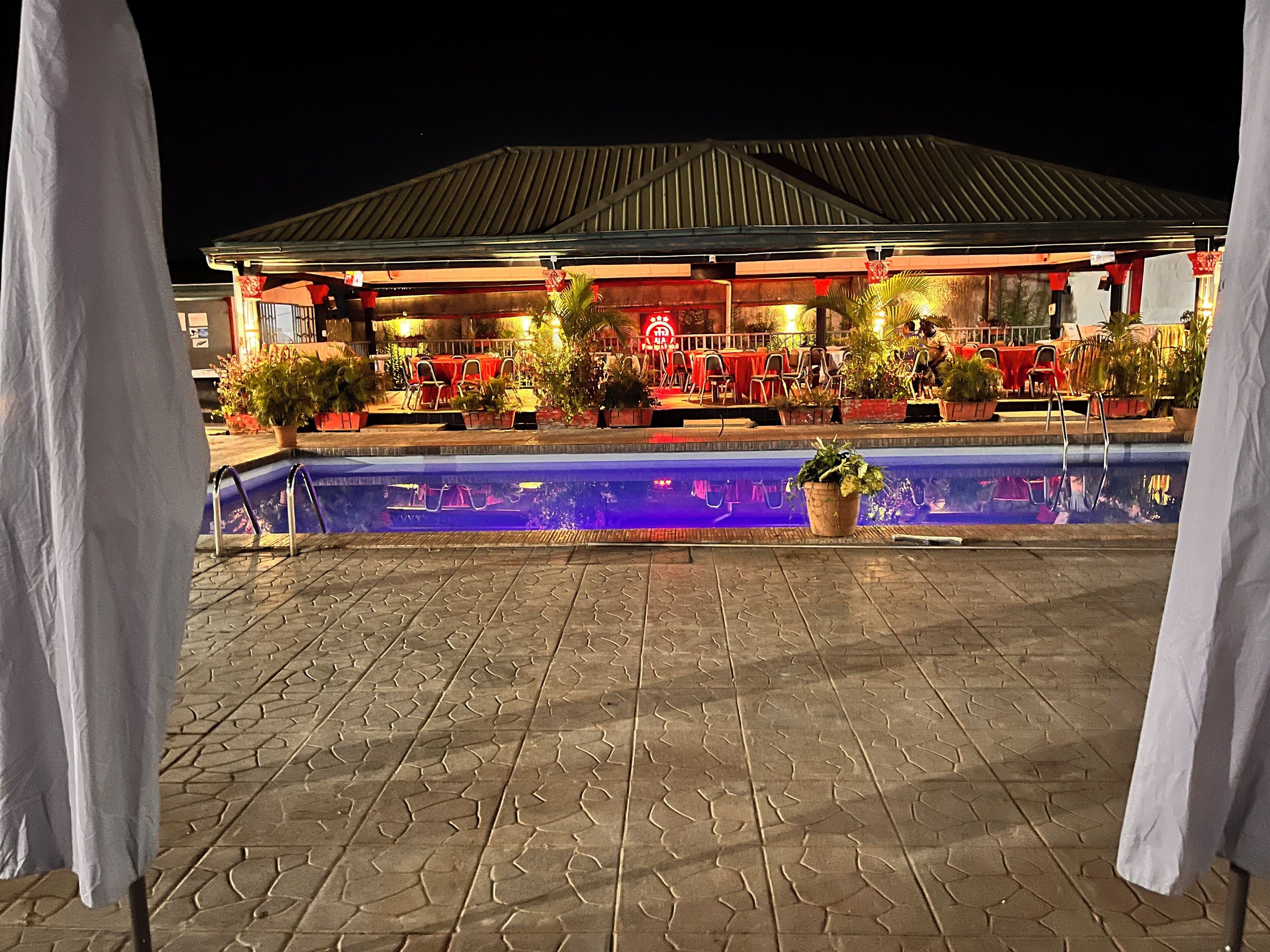 An outdoor pool area with a covered seating area and potted plants.