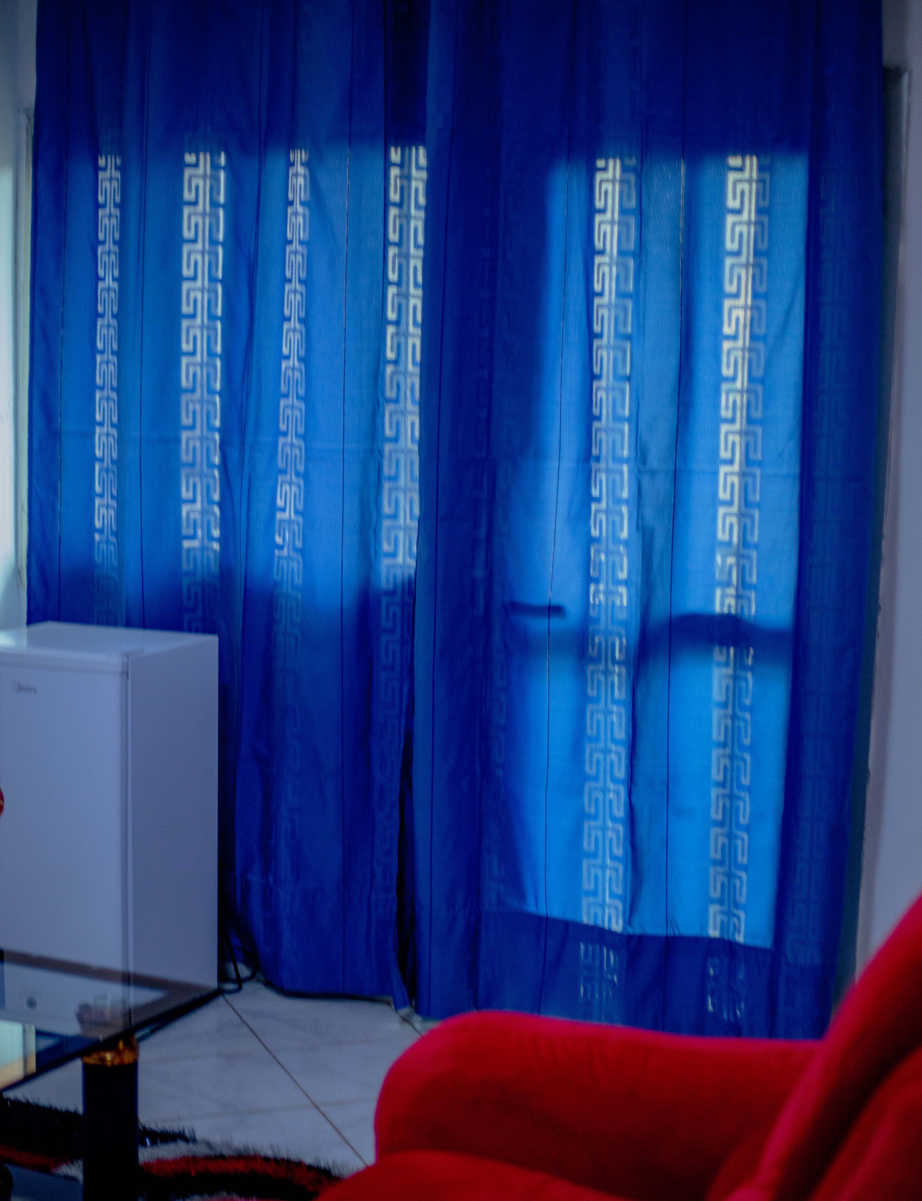 Una habitación con un radiador blanco, cortinas azules con un diseño geométrico y un sofá rojo.