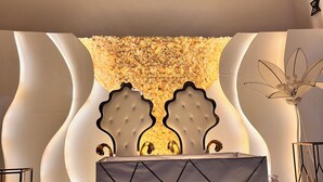 Een receptiebalie met een bord waarop 'Prodiges Hotel' staat, en een decoratieve achtergrond met bloemstukken en een kroonluchter.