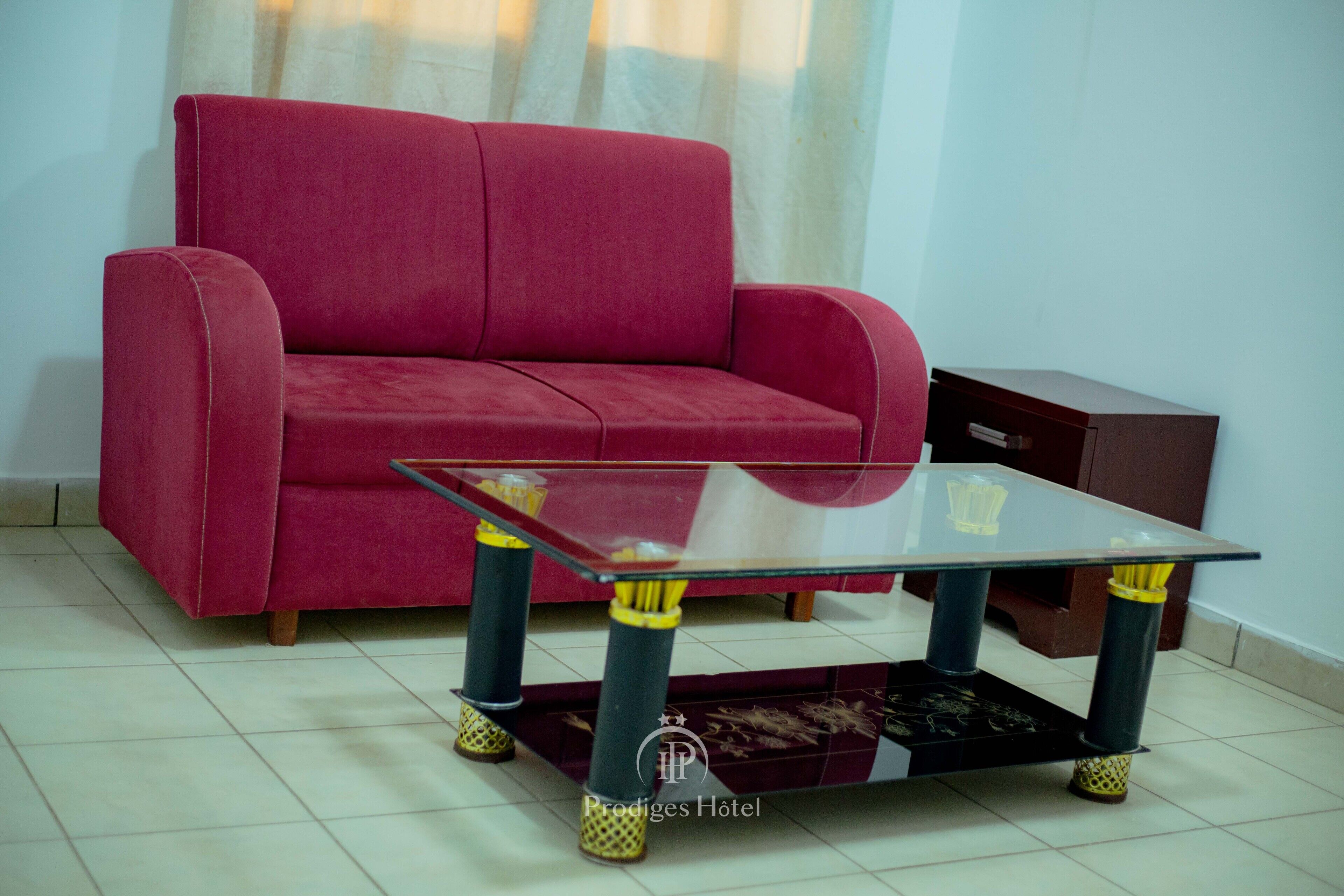 A red sofa and a glass-top table with yellow accents in a room with tiled flooring.