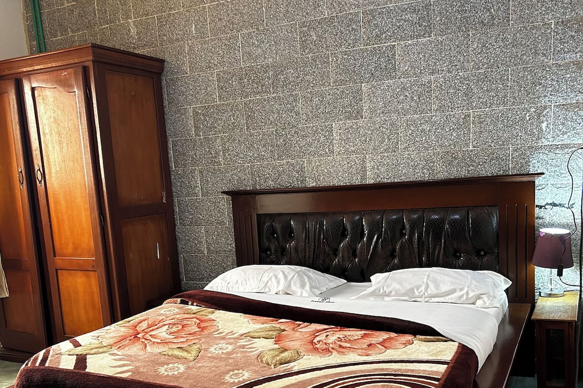 A bedroom with a bed, a wooden wardrobe, a telephone, and a patterned bedspread.
