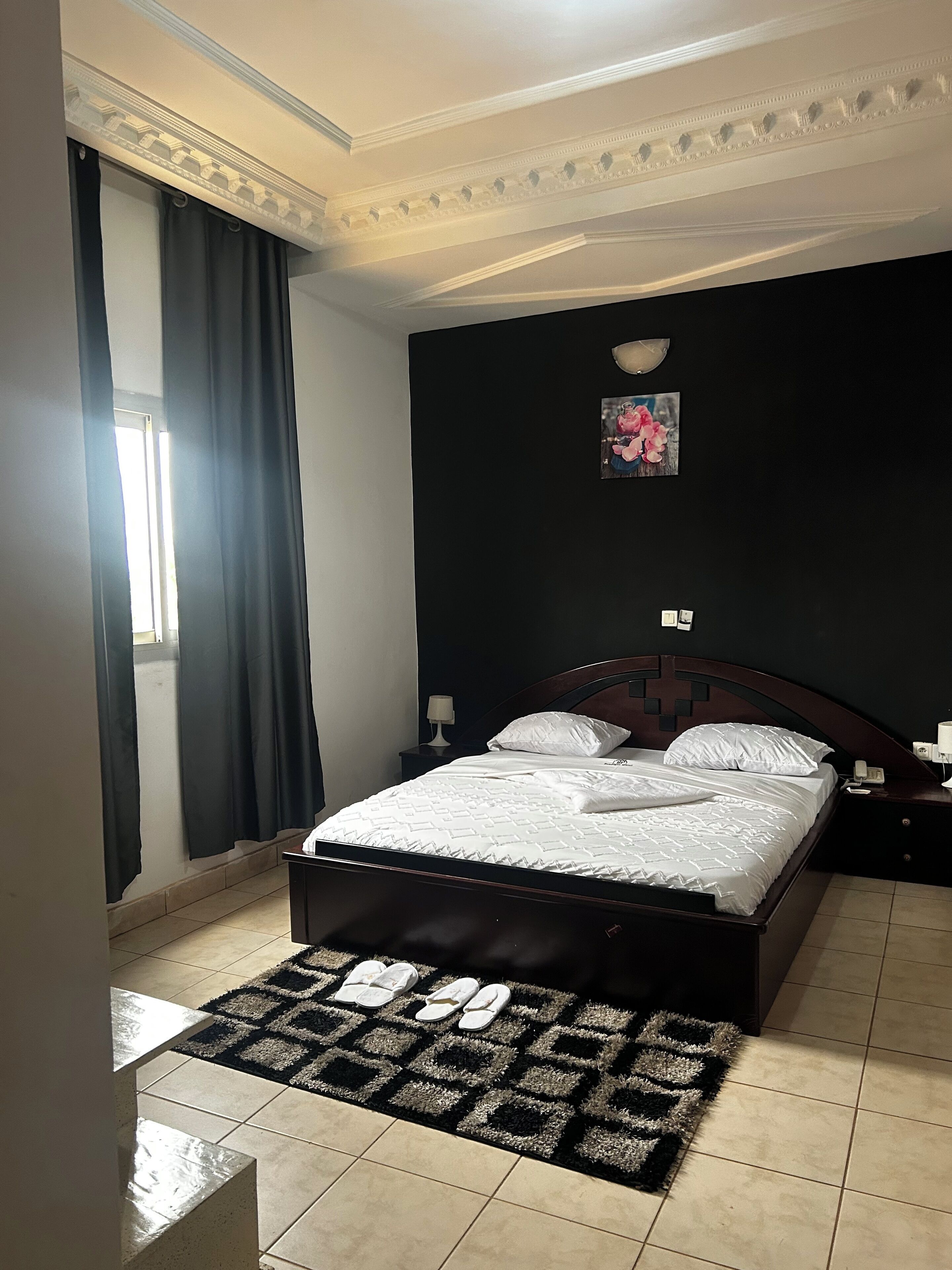 Een slaapkamer met een bed, donkere gordijnen, een lijst met een afbeelding, een nachtkastje en een vloerkleed.