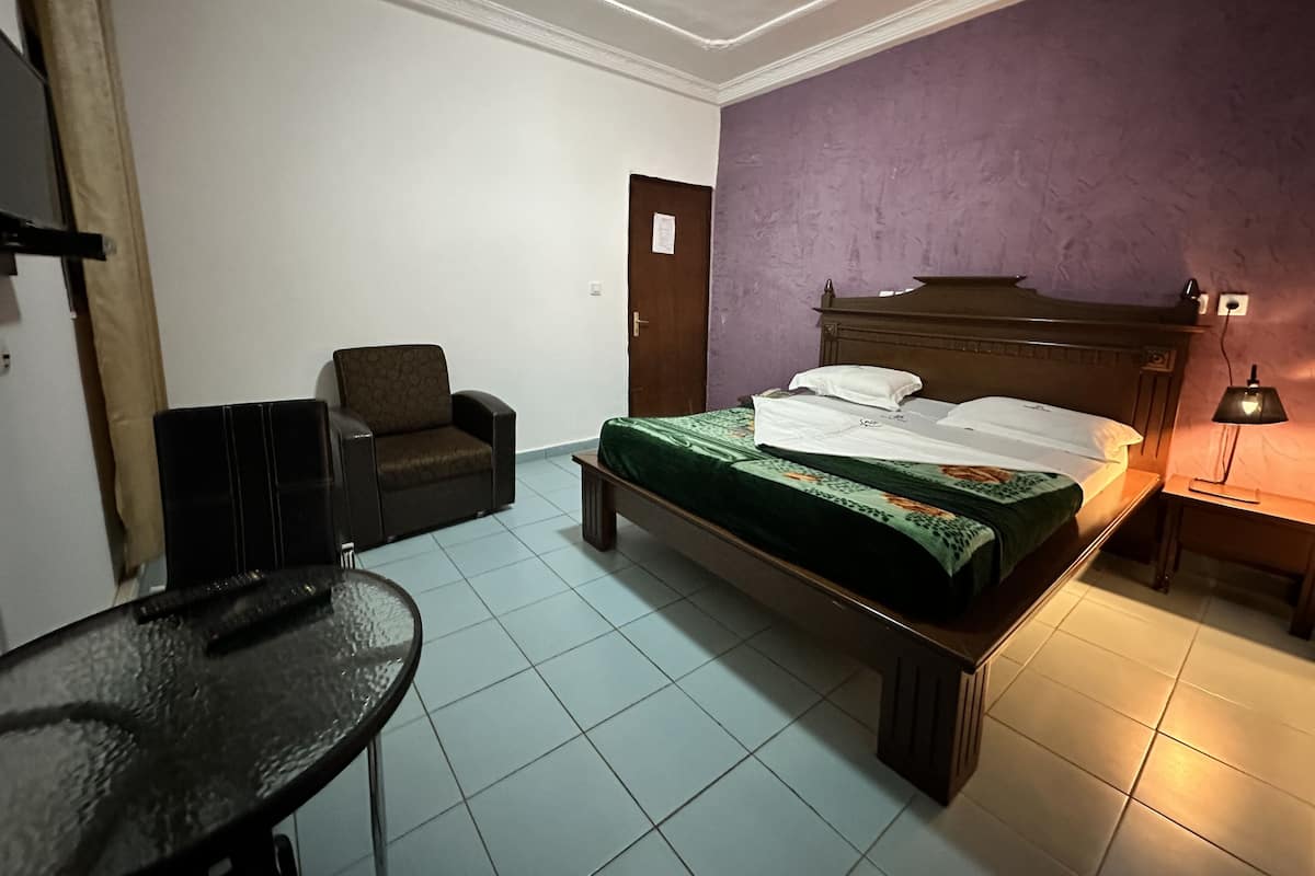 A bedroom with a bed, a chair, a table, and a door.