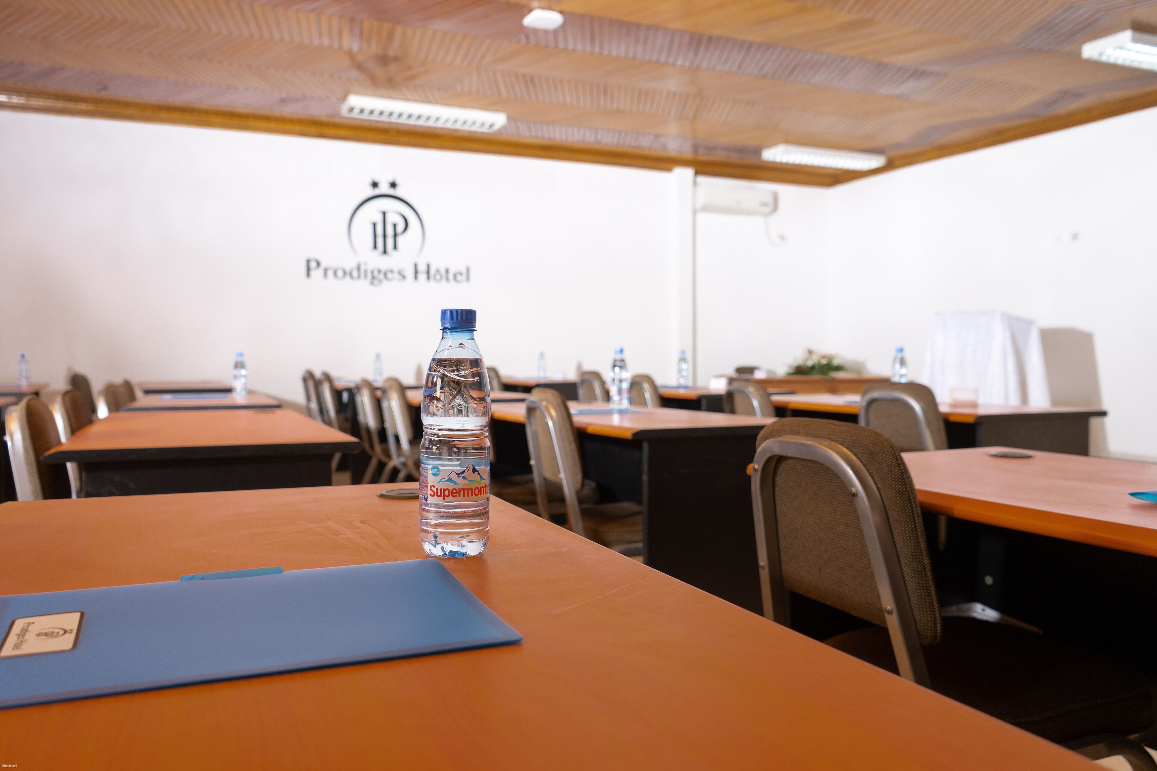 Un salón de conferencias con mesas, sillas y una botella de agua sobre una de ellas.